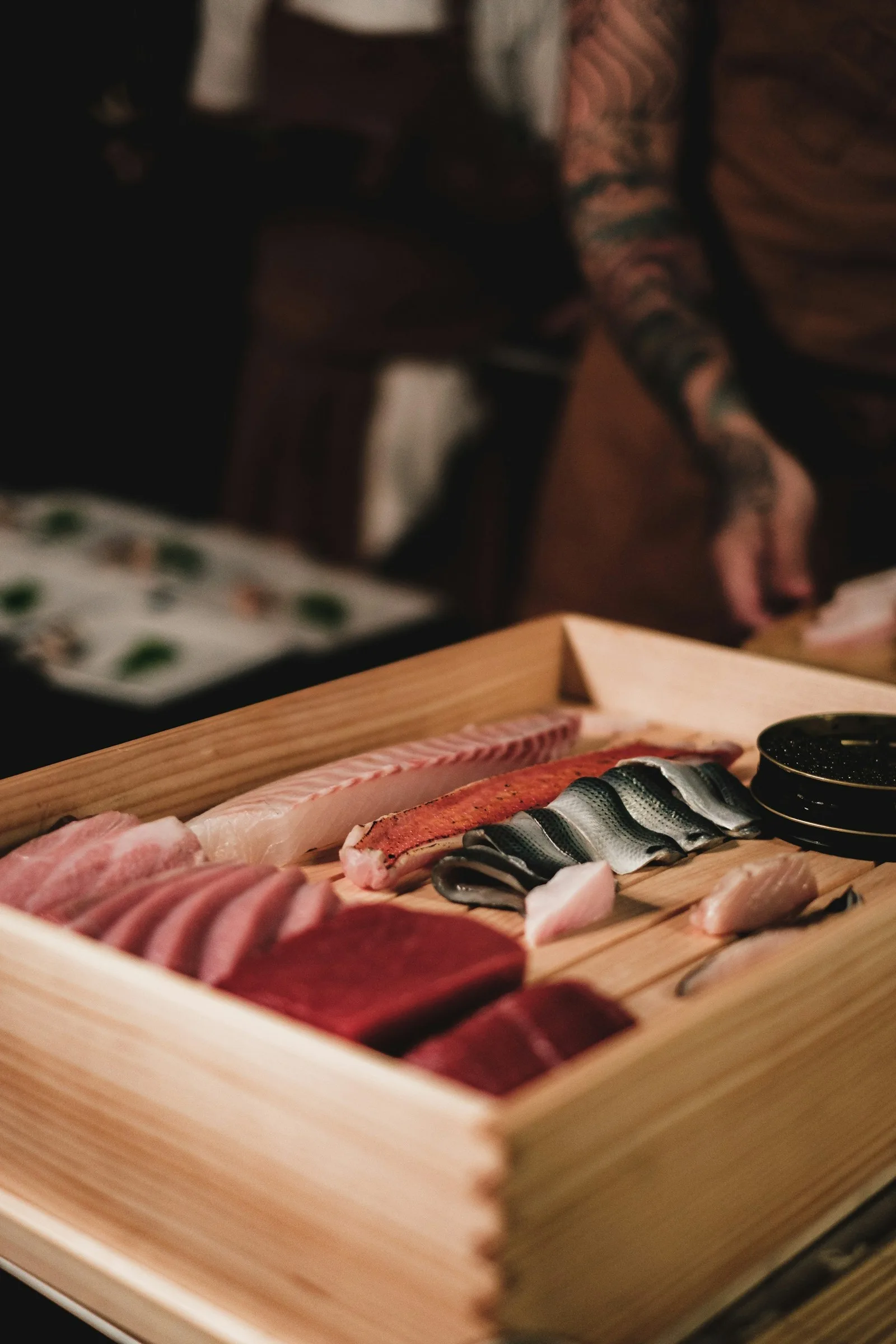 A wooden omakase box filled with assorted nigiri on a black background