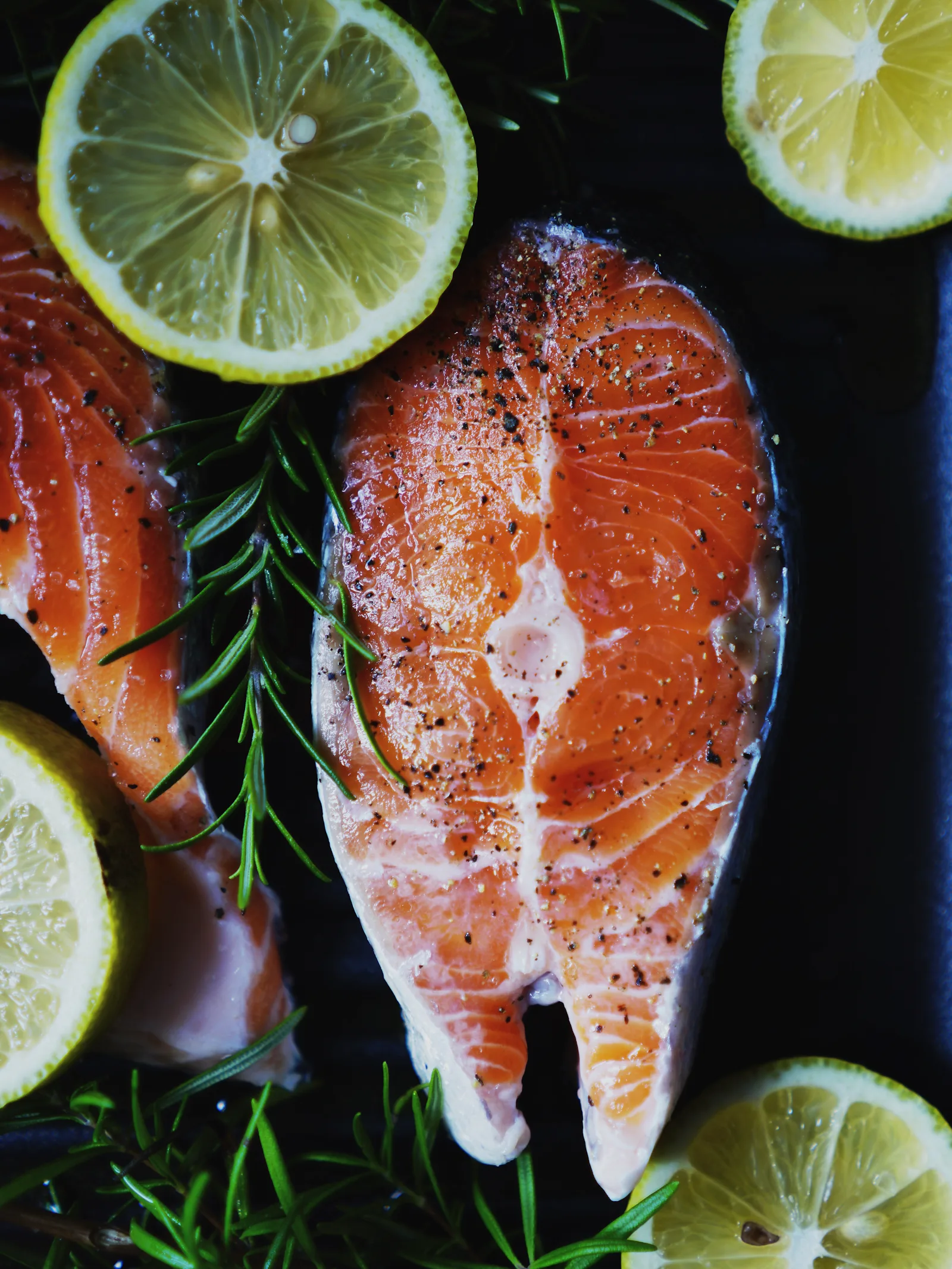 Fresh salmon steaks with lemon slices and rosemary on a dark tray