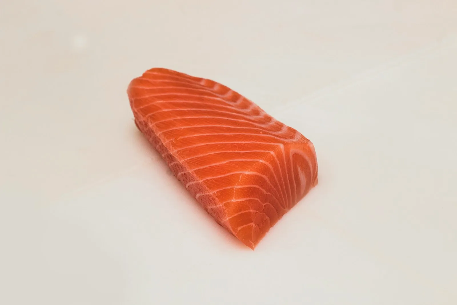 A perfectly trimmed block of salmon on a white cutting board